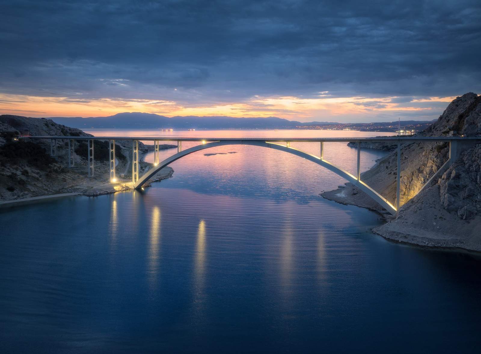 Bridge over calm sea at sunset — quiet arch reflected in still water
